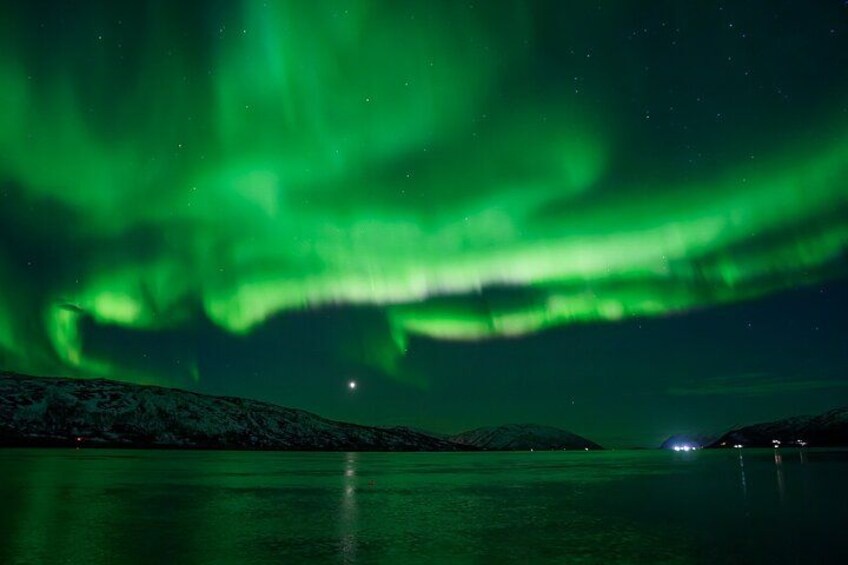 Nordlys over en rolig sø med sneklædte bakker i baggrunden. 3
