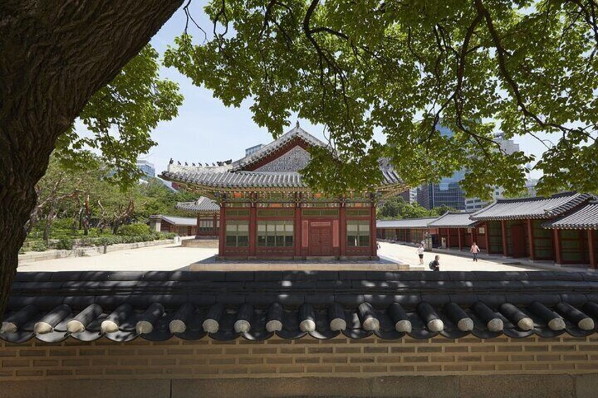A traditional Korean building with a tiled roof, surrounded by a brick wall and a tree-lined pathway. 1