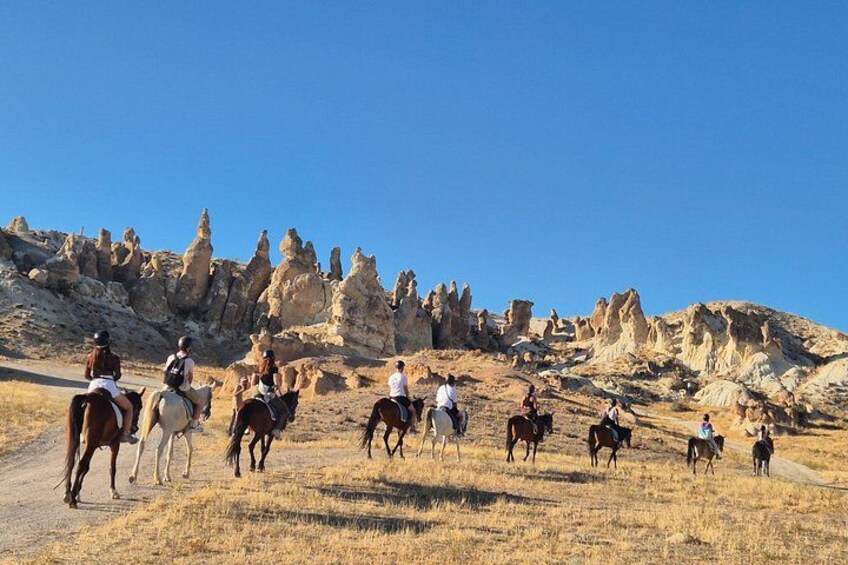 A group of people riding horses on a dirt path with unique rock formations in the background. 3