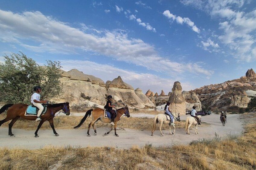 A group of people riding horses on a paved path through a desert landscape with distinctive rock formations. 1