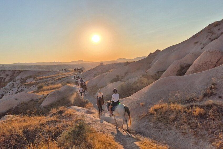 A group of people horseback riding on a trail during sunset. 4