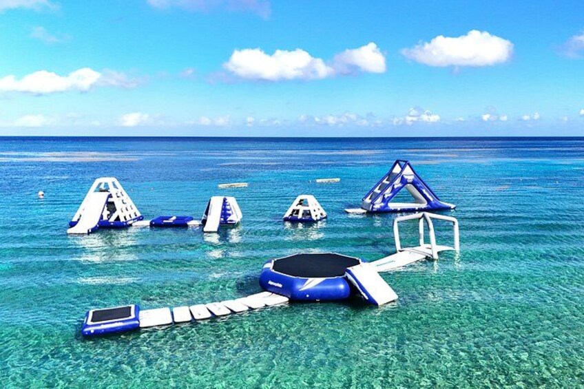 A clear blue sea with floating structures, including a blue inflatable raft and a white raft with a blue canopy. 2