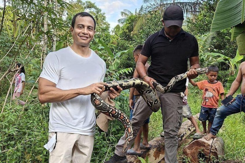 A person holding a large snake, surrounded by people in a lush, green environment. 3