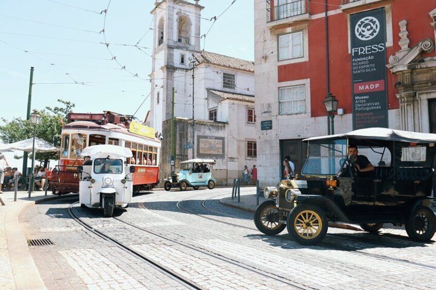 Una calle con tranvías, un coche antiguo y un edificio con una torre de reloj. 3