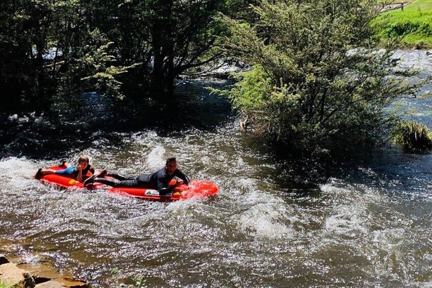 Två personer i en röd flotte på en flod, omgiven av träd. 3