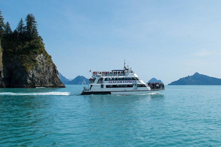 Un crucero blanco llamado Glacier Express navega sobre aguas azules cristalinas, con una costa montañosa al fondo. 3