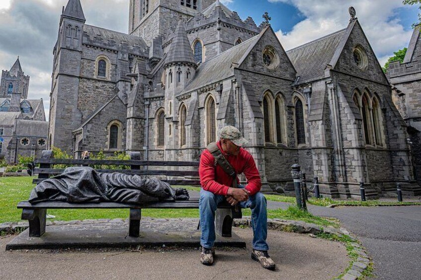 A man sitting on a bench in front of a large stone church with a statue nearby. 1