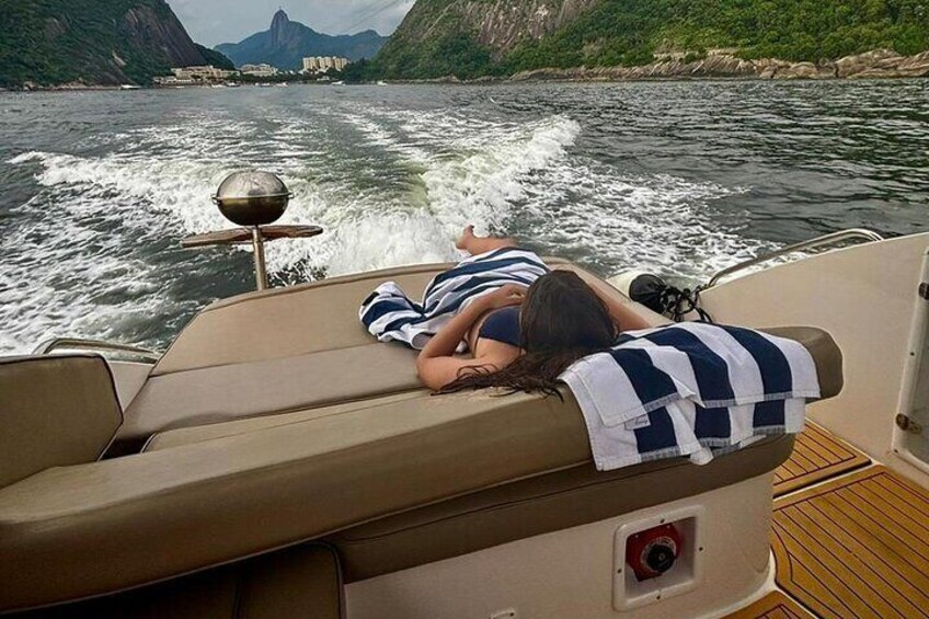 Un bote con dos personas recostadas en sillones de sol, un rastro de agua detrás y un paisaje montañoso al fondo. 5