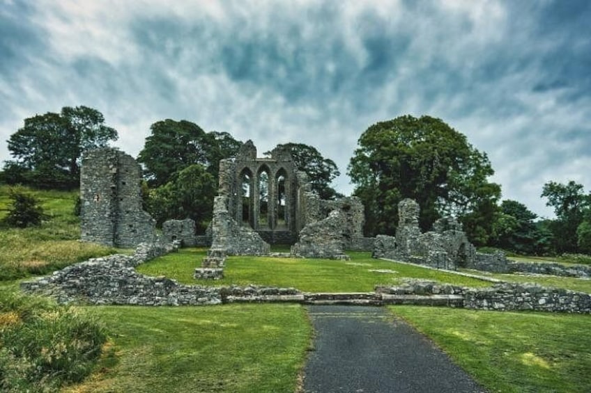A ruined stone structure with arches, surrounded by grass and trees under a cloudy sky. 1