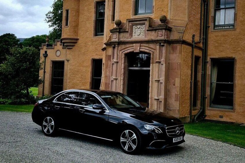 A black Mercedes-Benz parked in front of a historic building with a stone facade and arched windows. 1