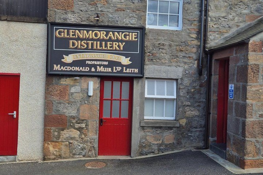 A stone building with a sign for Glenmorangie Distillery, red doors, and a small window. 2