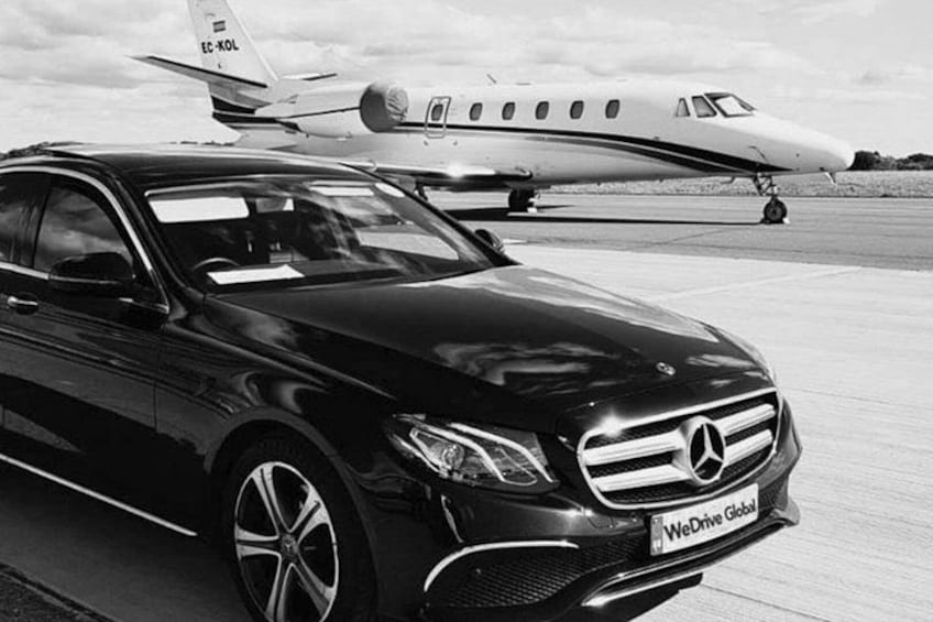 A black Mercedes-Benz car parked in front of a private jet on a tarmac. 4