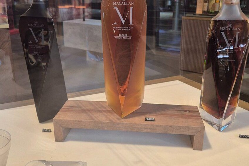 Three Macallan VI whiskey bottles on a wooden display stand. 3
