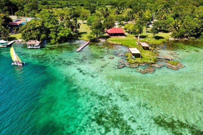 An aerial view of a tropical island with clear turquoise waters, a small boat, and a few structures including a red-roofed building. 4