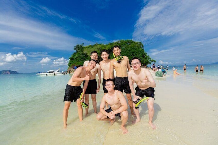 A group of people on a beach with clear water and a boat in the background. 1