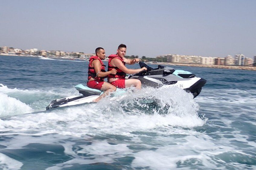 Deux personnes font du jet-ski sur une étendue d’eau, avec des bâtiments en arrière-plan. 2