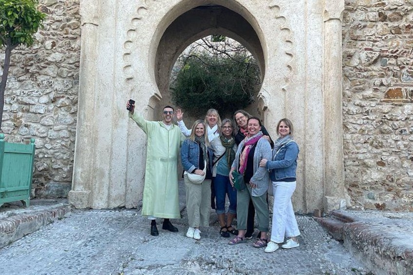 A group of people posing in front of a stone archway with a tree in the background. 1