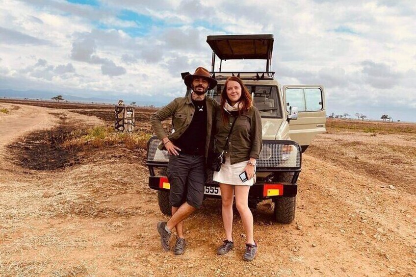 A man and a woman standing in front of a safari vehicle on a dirt road. 2