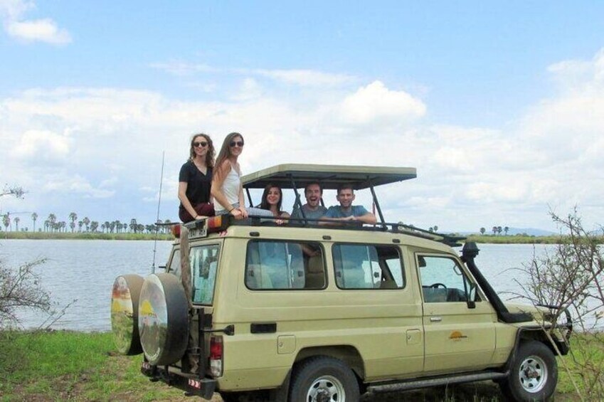 A beige off-road vehicle parked by a lake with four people on top. 5