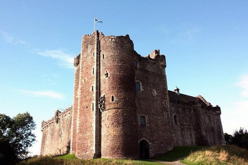 A large, historic stone castle with a prominent tower, a flag, and a grassy foreground. 3