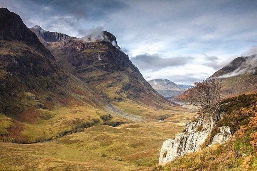 A mountainous landscape with a valley, rocky outcrops, and a clear sky. 1