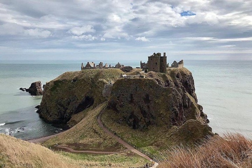 A coastal landscape with a castle on a grassy cliff overlooking the sea. 3