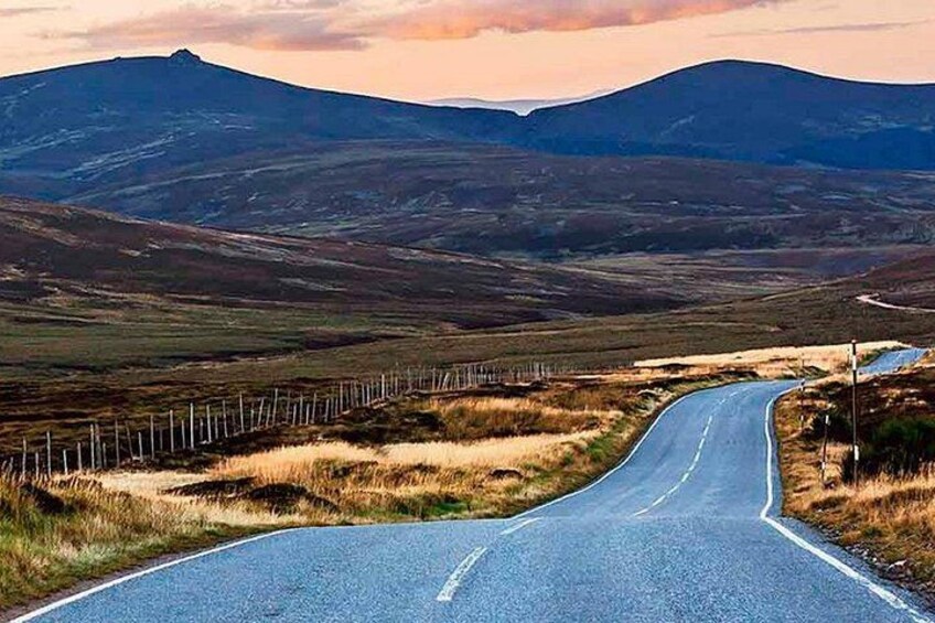 A winding road through a hilly landscape with a fence on one side and a mountain in the background. 2