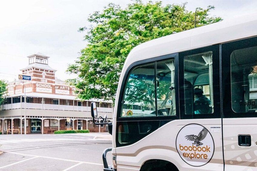 Ein weißer Bus mit 'boobook explore'-Branding vor einem Gebäude, an dem '1918 SCHOOL OF ARTS' steht. 5