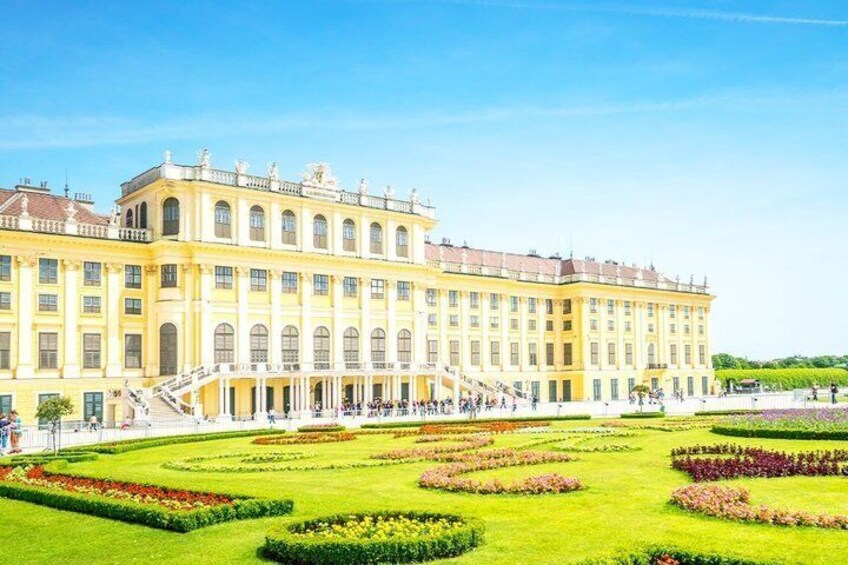 A large classical building with a symmetrical facade, a central staircase, and a well-manicured garden with geometric flower beds. 3