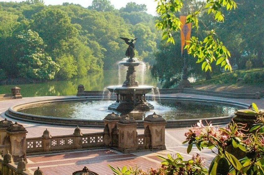 A circular fountain with a statue, surrounded by a stone fence and lush greenery. 2