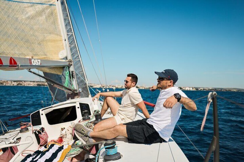 Deux personnes à bord d’un voilier, avec un ciel bleu dégagé et une mer calme en arrière-plan. 2
