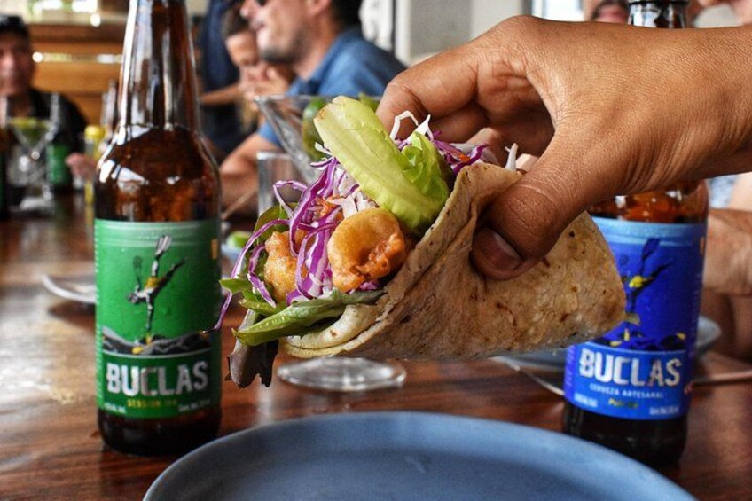 A hand holding a taco with lettuce and a sauce bottle labeled 'BULLAS' in the background. 2