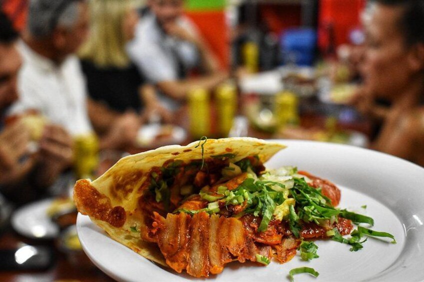 A taco with crispy bacon and fresh greens on a white plate. 3