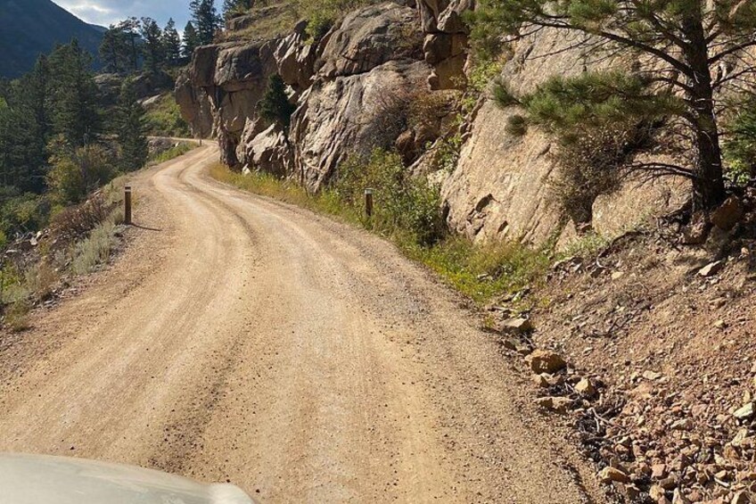 A winding dirt road in a mountainous area with rocky cliffs and sparse vegetation. 1