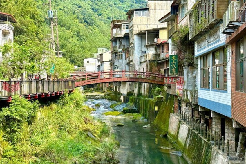 A narrow river, a wooden bridge, and buildings along the riverbank. 3