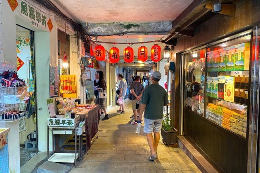 A narrow alley with shops, red lanterns, and people walking. 2