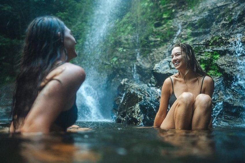 Two people sitting by a waterfall in a natural setting. 2