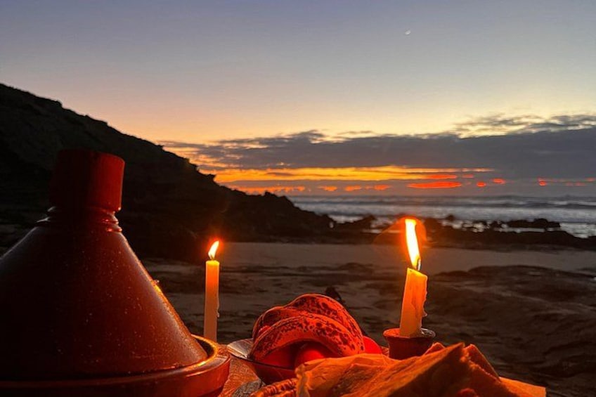 A sunset over a beach with two lit candles and a red object on the sand. 4
