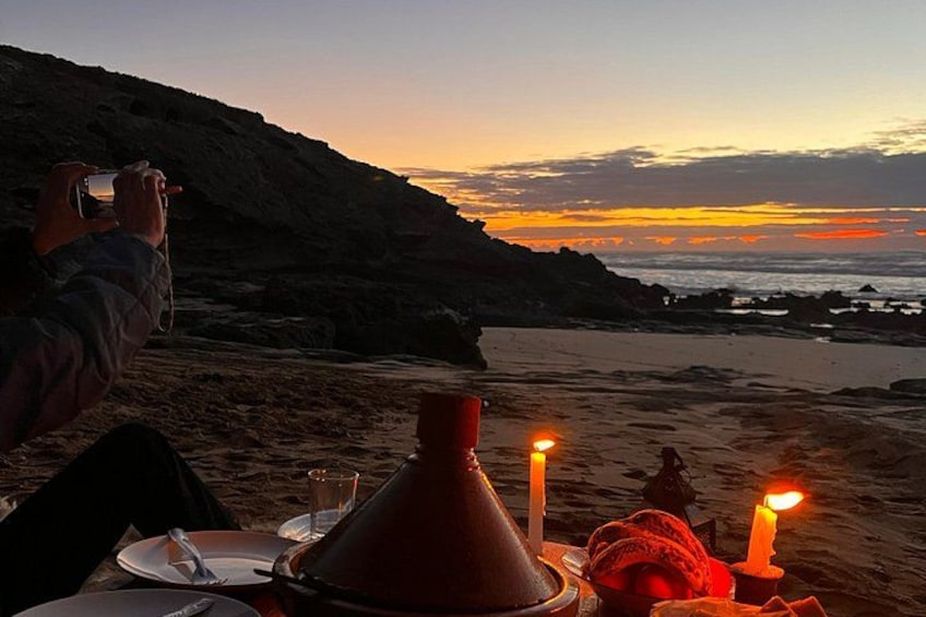 A beach scene with a sunset, a person taking a photo, and a table with a candle. 2