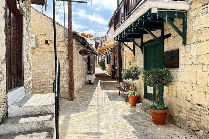 Una stretta via acciottolata con edifici in pietra, una panchina di legno e piante in vaso. 1