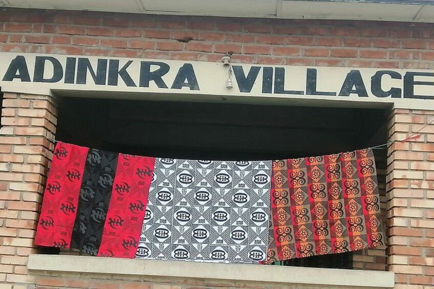 A storefront with the sign 'ADINKRA VILLAGE' and patterned fabrics hanging in front. 3