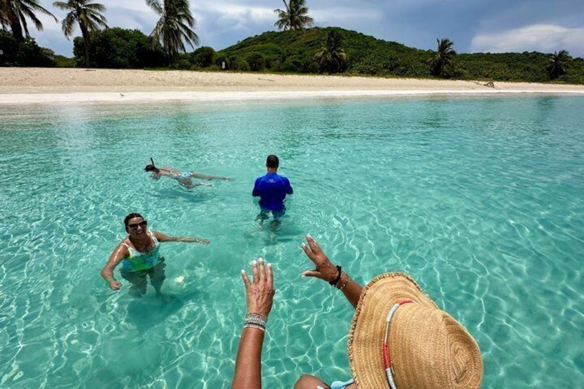 A clear turquoise sea with people swimming and a beach in the background. 4