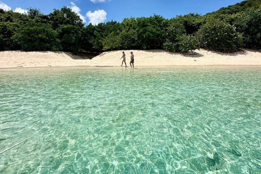 A beach with clear turquoise water and a person walking in the distance. 5