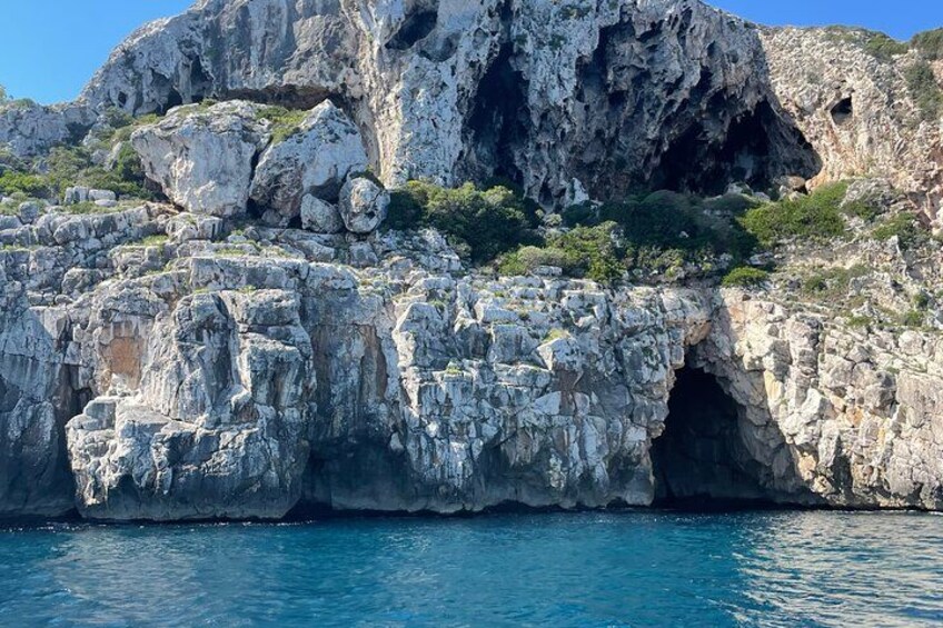 Una costa rocosa con la entrada de una cueva y agua azul cristalina. 4