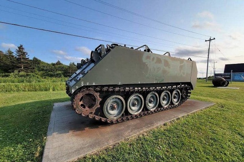A military tank on display outdoors with a grassy field and a paved path in the background. 5