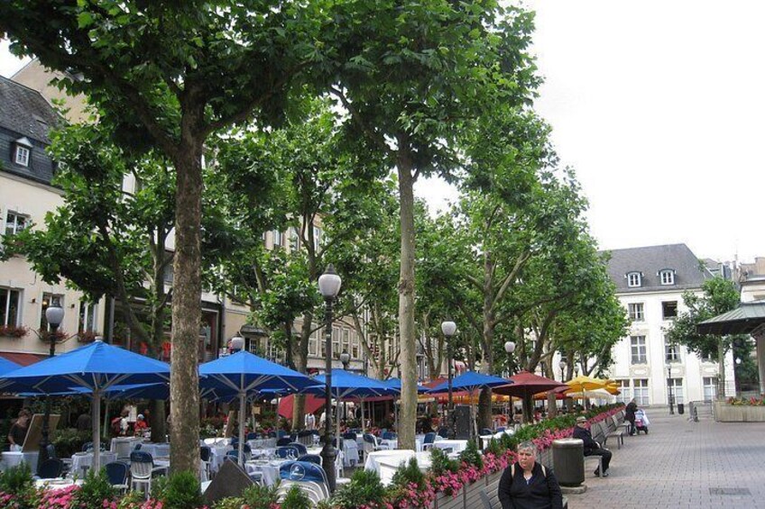 Outdoor seating with umbrellas, trees, and buildings in a town square. 2