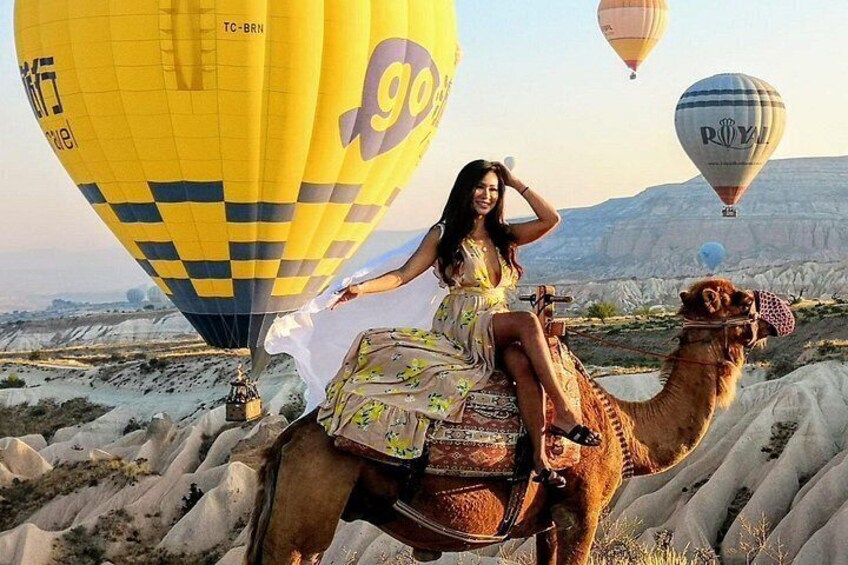 A camel with a rider in a dress, a yellow hot air balloon, and a camel with a red and white umbrella. 3