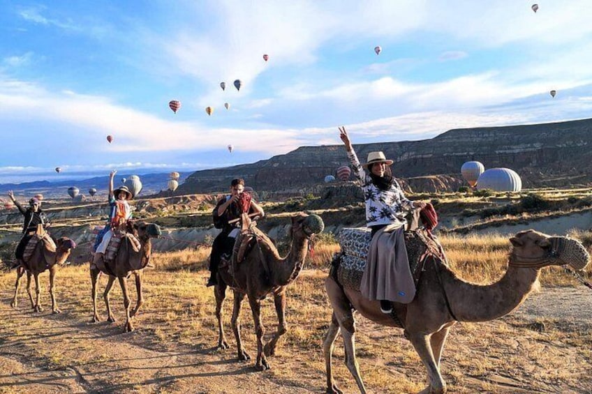 People riding camels in a desert with hot air balloons in the background. 2