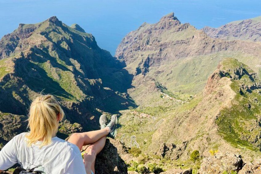 A person sitting on a rocky outcrop overlooking a mountainous landscape. 2