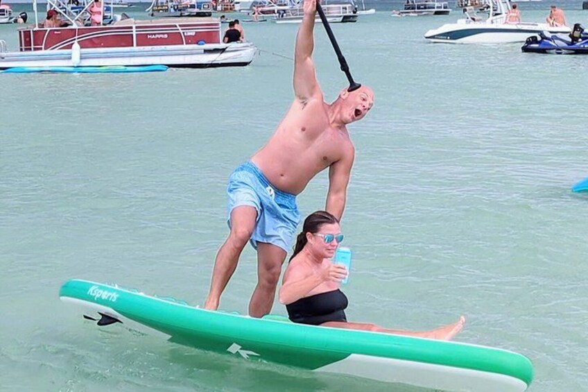 En mand står på et paddleboard, en kvinde sidder på en surfbræt, og en båd ligger i baggrunden. 2